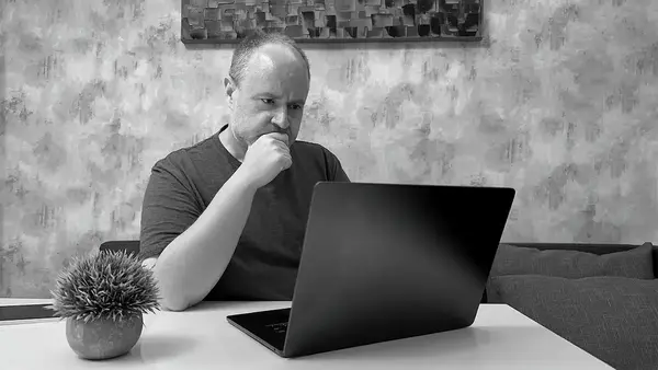 Person sitting at a table starring at a laptop computer intently.
