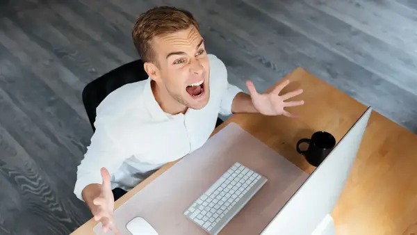 Person sitting at a desk with a laptop computer looking up in the air yelling in frustration.
