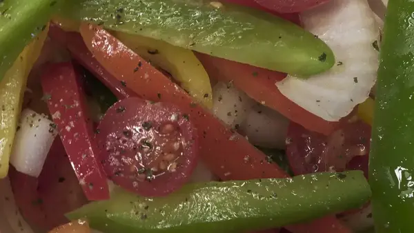 Close-up of a salad with sliced red, yellow, and green bell peppers, tomatoes, and onions.