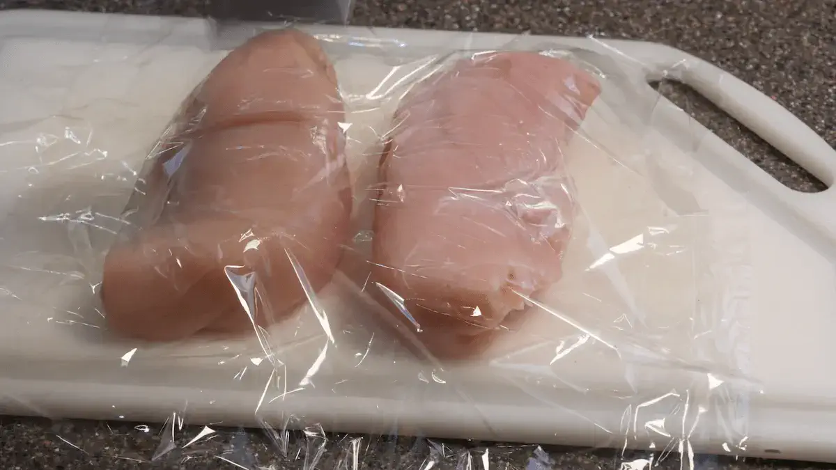 Two chicken breasts covered in plastic wrap